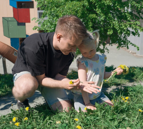 Mannlig barnehageansatt plukker blomster sammen med et barn i en barnehage