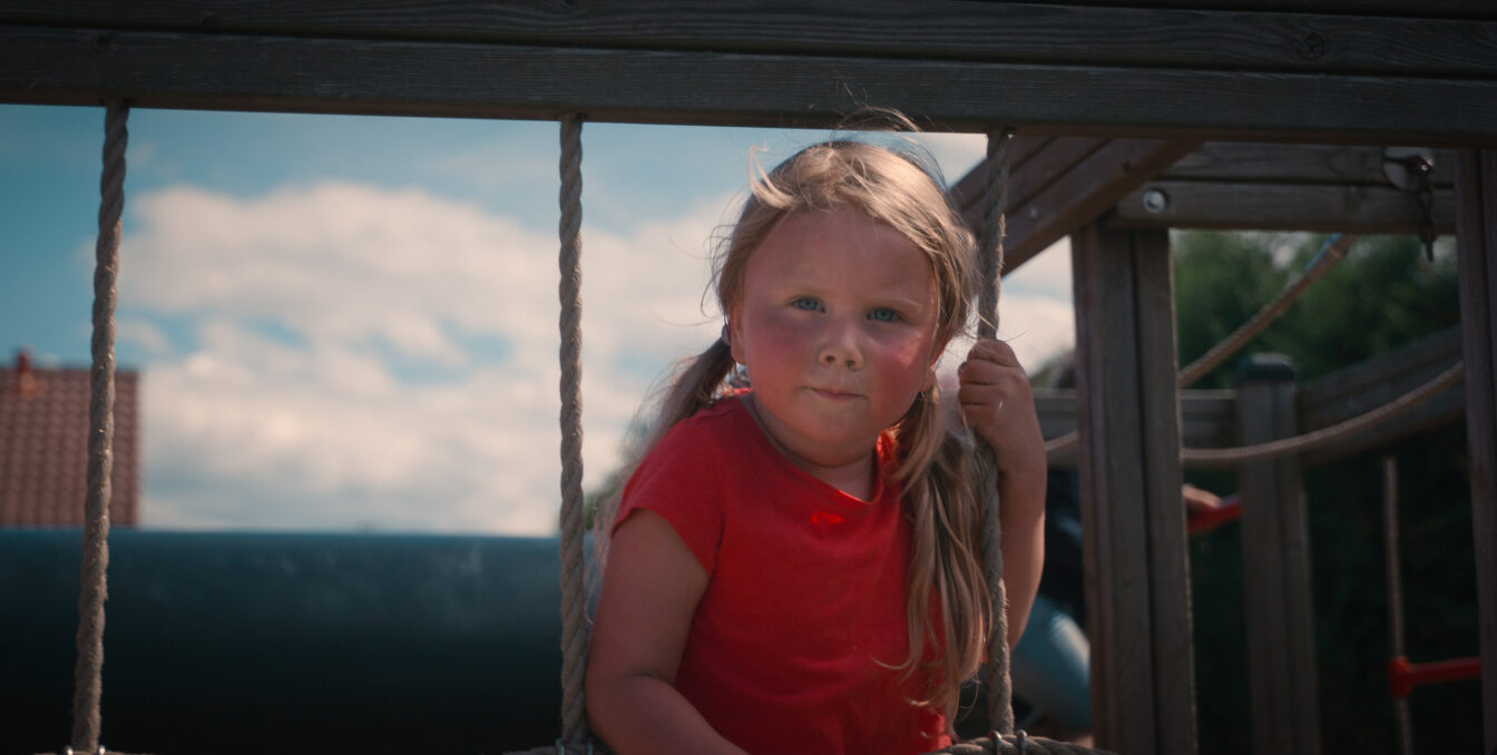 Jente ser inn i kamera mens hun klatrer i et lekestativnett