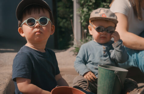 To barn med solbriller sitter i en sandkasse og leker