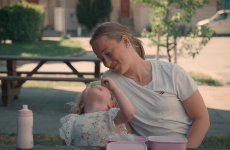 Liten jente spiser eple og ser på en voksen med nysgjerrige øyne.