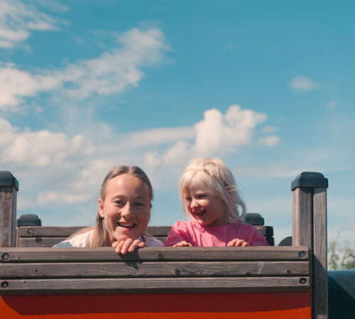 Kvinne og liten jente leker oppe i en sklie