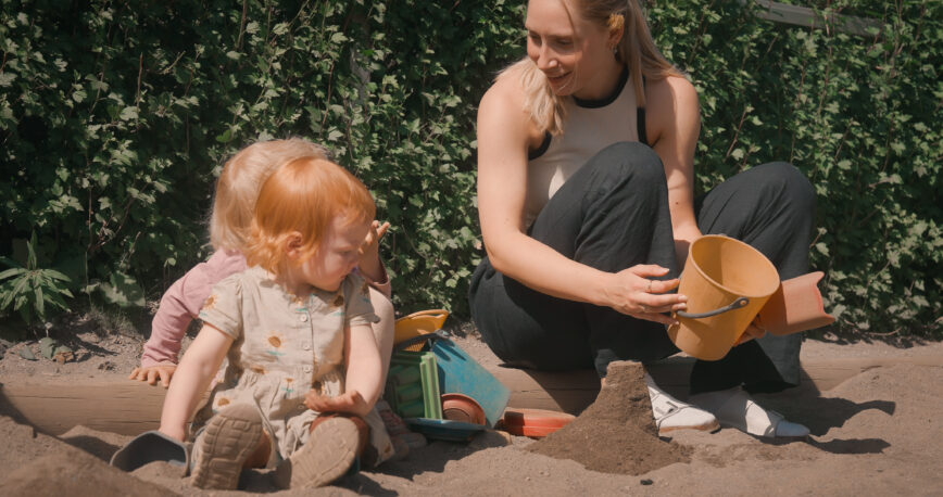To barn leker med en barnehageansatt i en sandkasse