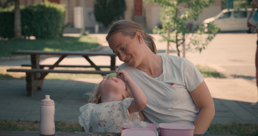 Liten jente spiser eple og ser på en voksen med nysgjerrige øyne.