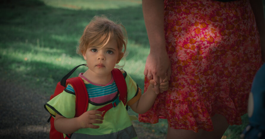 Jente i refleksvest og ryggsekk leier en kvinne med en rød kjole. Ser undrende mot kamera.