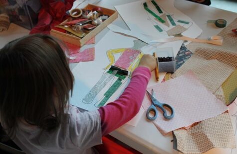 Dette er et bilde av et barnehagebarn ved et tegnebord som tegner og lager collage.