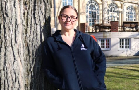 Joggebukse mørk blå Kvinnelig student lener seg mot et tre foran hovedbygget, kledd i DMMH hettejakke og joggebukse.