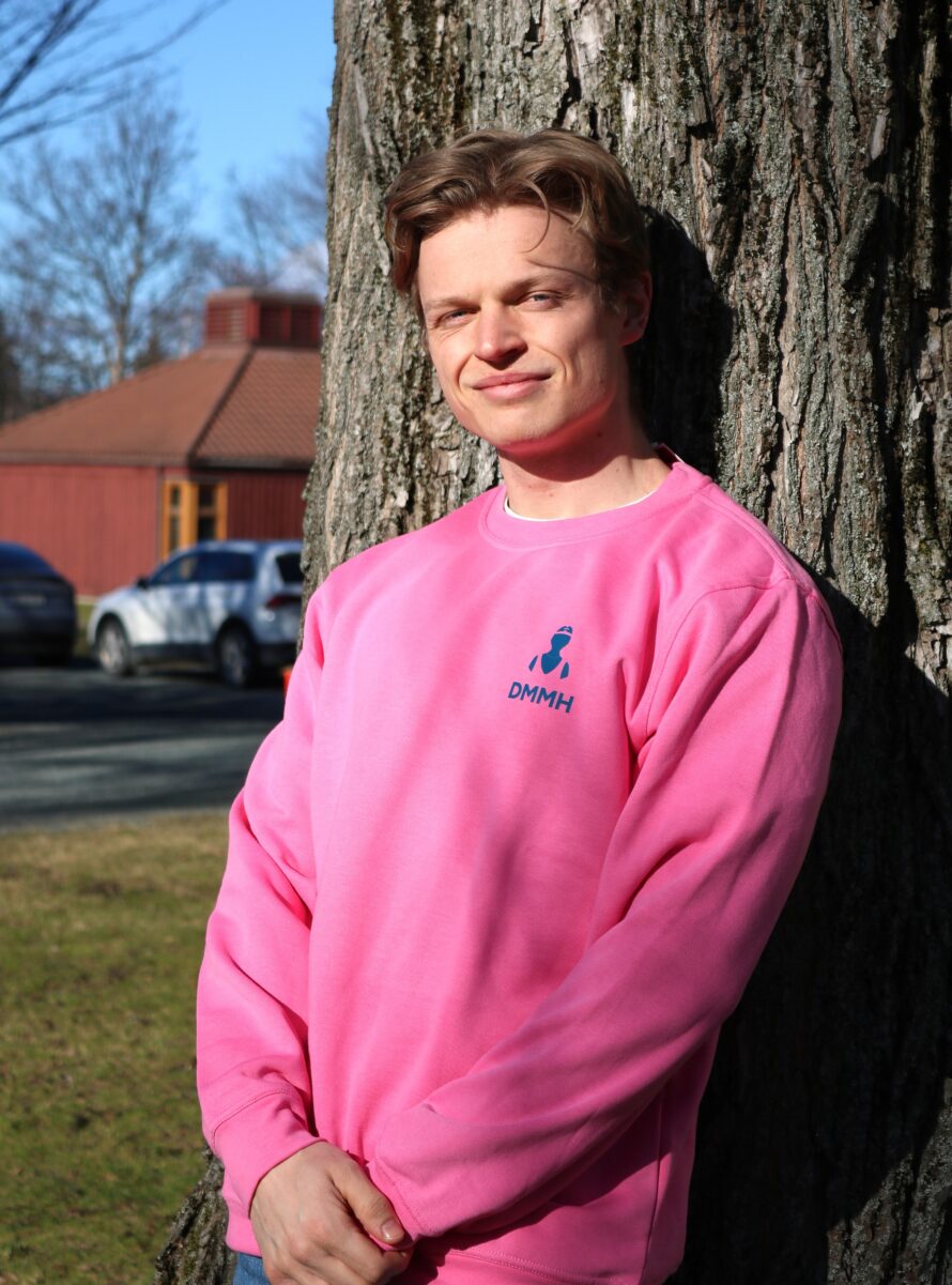 Mannlig student lener seg mot et tre i en rosa DMMH college geneser