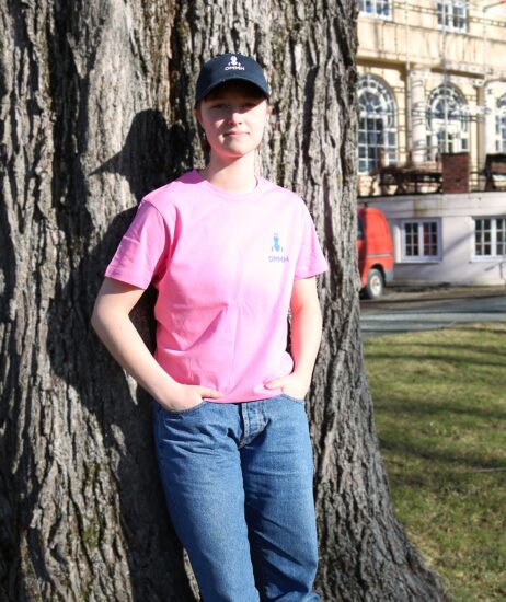 Kvinnelig student med en rosa DMMH t skjorte lener seg mot et tre.