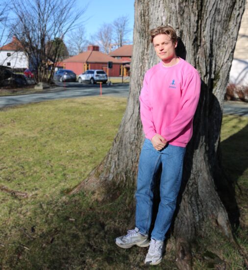 Mannlig student lener seg mot et tre i en rosa DMMH college geneser