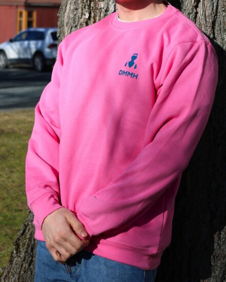 Mannlig student lener seg mot et tre i en rosa DMMH college geneser