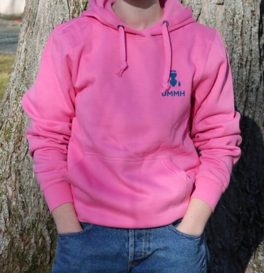 Bilde av en student i en rosa DMMH hettegenser foran et tre i parken foran hovedbygget.