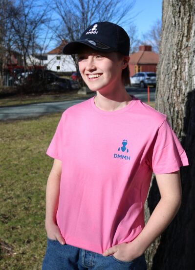 Kvinnelig student med en rosa DMMH t skjorte lener seg mot et tre.