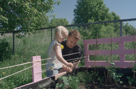 Lars Moe viser en liten jente noen voksende planter i et bed