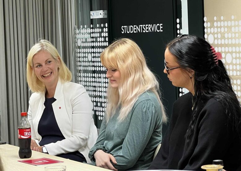 En kvinne fotografert forfra, i samtale med to kvinner fotografert sidelengs.