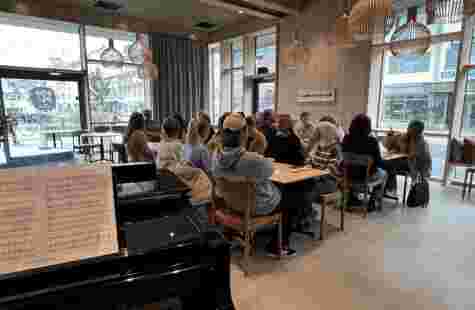 Bilde av et halvt piano og studenter som sitter i et klasserom.