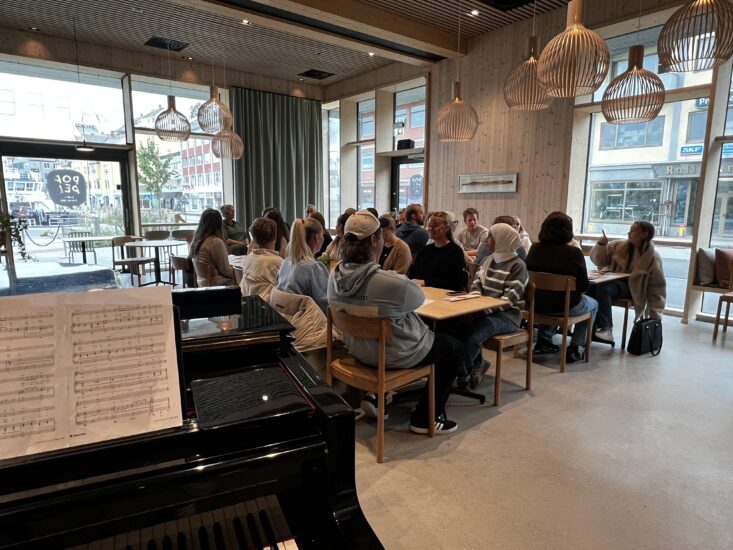 Bilde av et halvt piano og studenter som sitter i et klasserom.