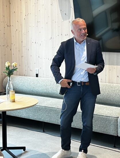 En mann med ordførerkjede står ved siden av et bord med en vase med 3 gule roser.