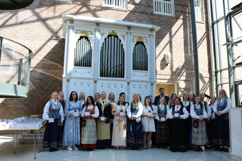 En rekke av unge mennesker i bunad og festklær, inne på DMMH.