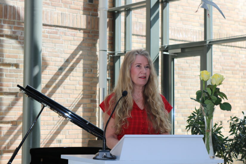 En kvinne står på en talerstol, bak 3 gule roser.