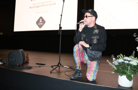 Barnehagen for en ny tid - engasjerende konferanse i Trondheim En mann med tights, cap og solbrikker kneler på en scene og synger i mikrofon