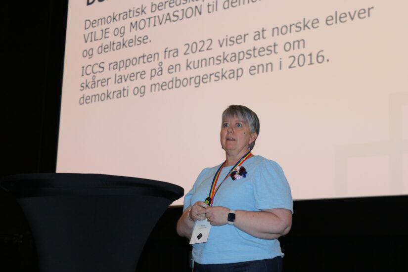 En kvinne står foran en skjerm og taler