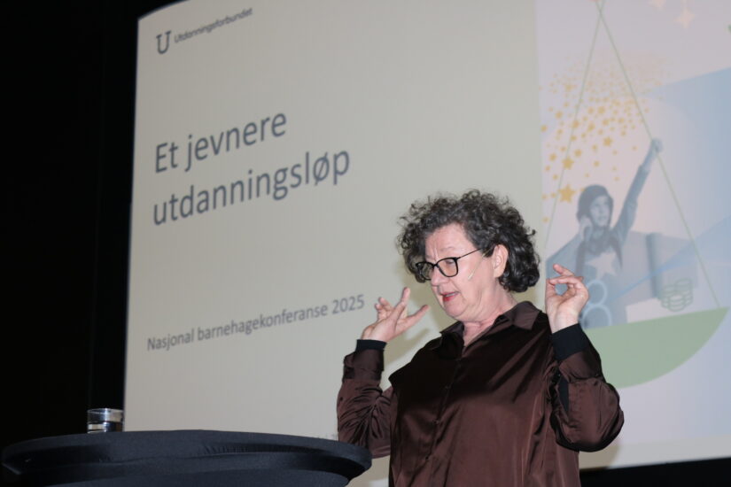 En kvinne står foran en skjerm og snakker