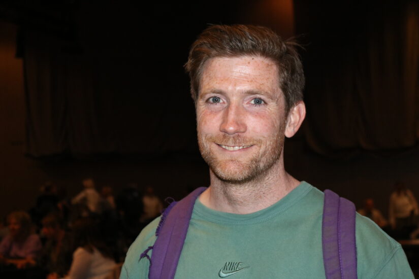 En mann står foran en sal der det sitter mennesker