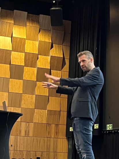 En mann snakker engasjert oppe på en scene.