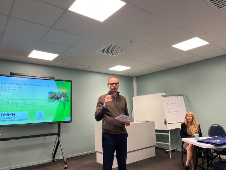 En mann står med mikrofon foran en skjerm.