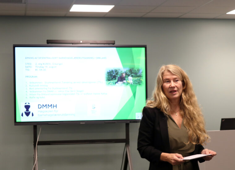 En kvinne står foran en skjerm og snakker.