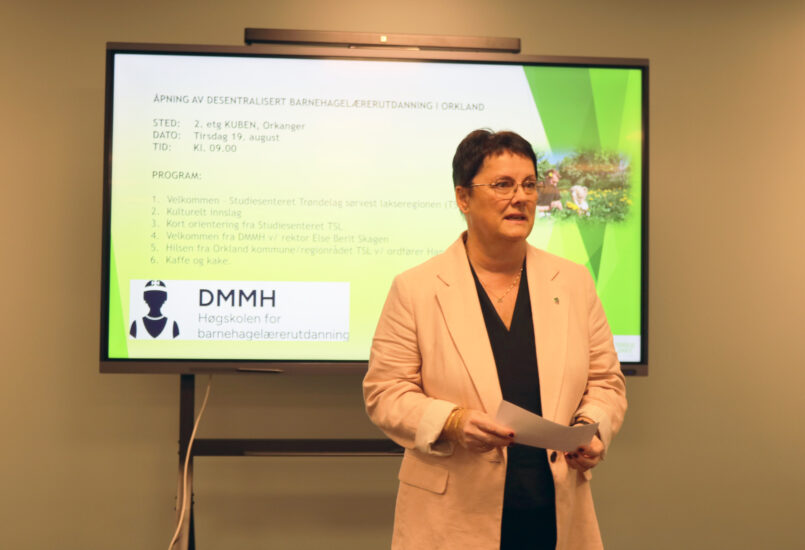 En kvinne står foran en skjerm og snakker.