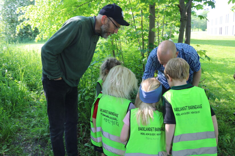 To menn og flere barn står samlet og ser ned på noe.