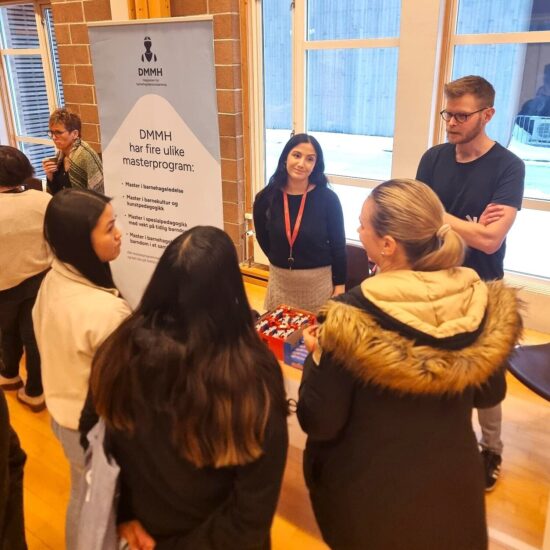 To ansatte ved Dronning Maud i samtale med studenter ved stand i gymsalen.