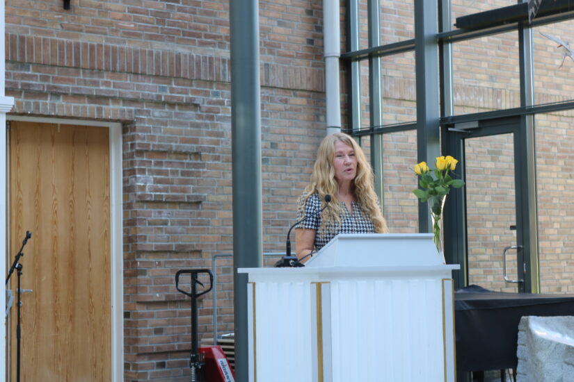 En kvinne står bak en talerstol og snakker i mikrofon.