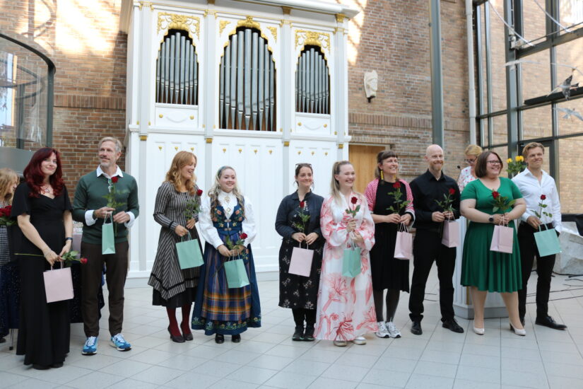 Glade mennesker i pene klær står med gaveposer i hendene.