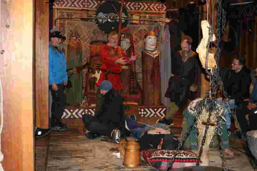 En mann i vikingdrakt står sammen med noen andre menn, rundt et hengende bål.