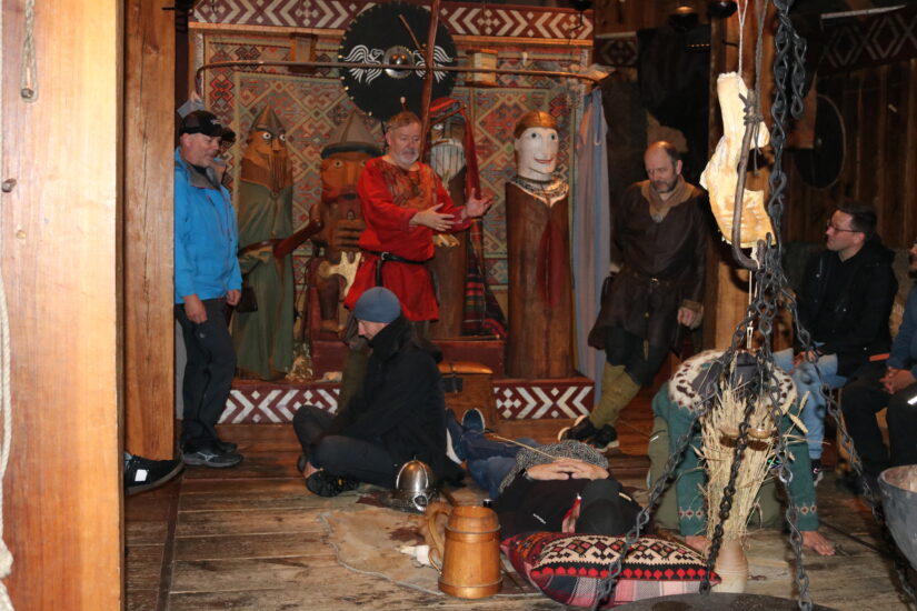 En mann i vikingdrakt står sammen med noen andre menn, rundt et hengende bål.