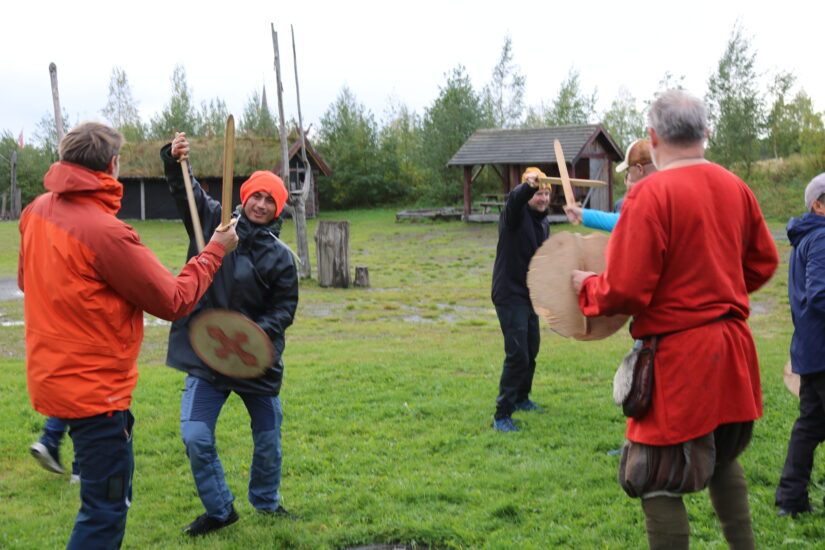 Flere menn slår mot hverandre med tresverd og skjold.