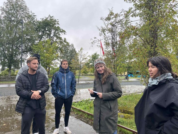 To kvinner står utendørs og snakker til menn.