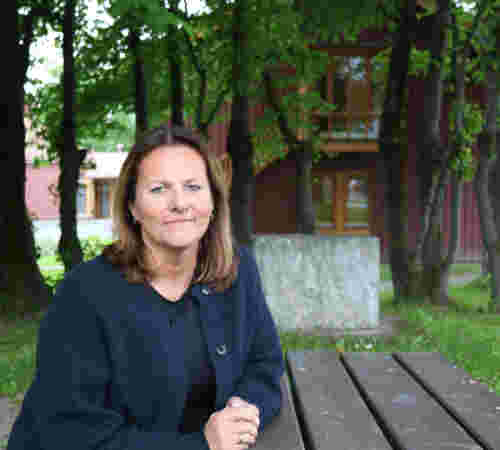 En kvinne sitter på en benk foran et rødt bygg.