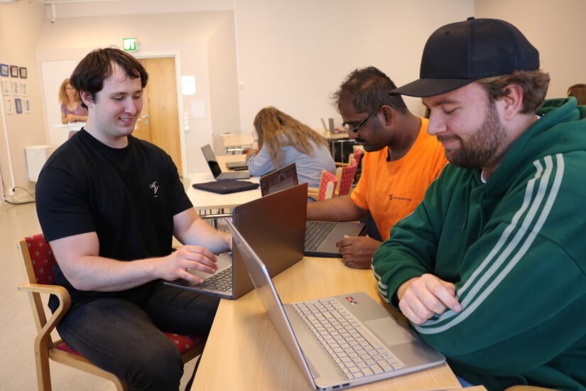 Tre unge menn sitter samlet rundt en pc.