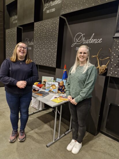 To kvinner viser fram noe materiale på et bord.