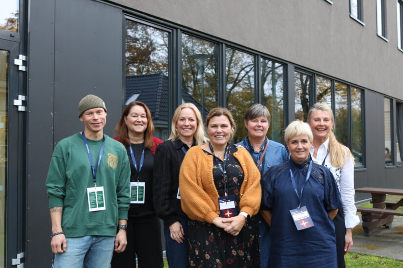 En gruppe mennesker fotografert foran en stor vegg.
