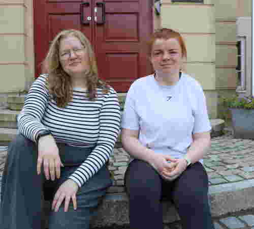 To unge kvinner sitter på trappa foran DMMH.