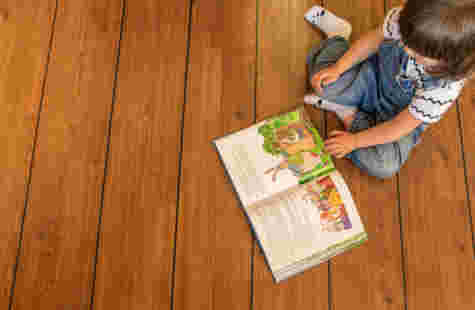 Et barn sitter på et tregulv og leser en bok