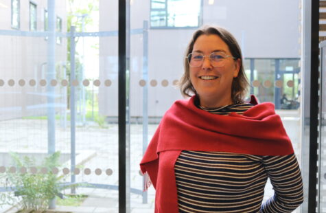 En kvinne med rødt sjal står foran et vindu.