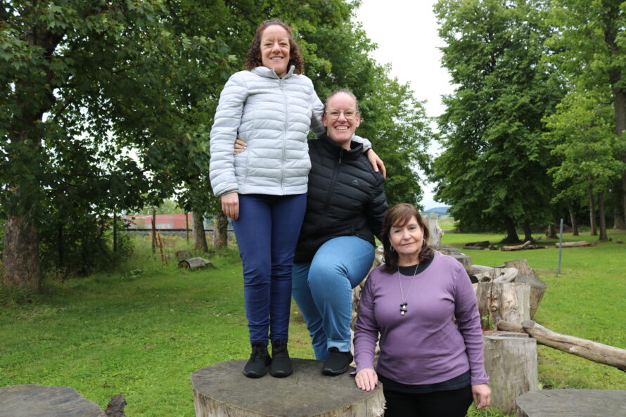 Three kvinner står oppe på trestubber.