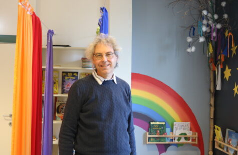 En mann står i et rom med regnbuefarger rundt seg.