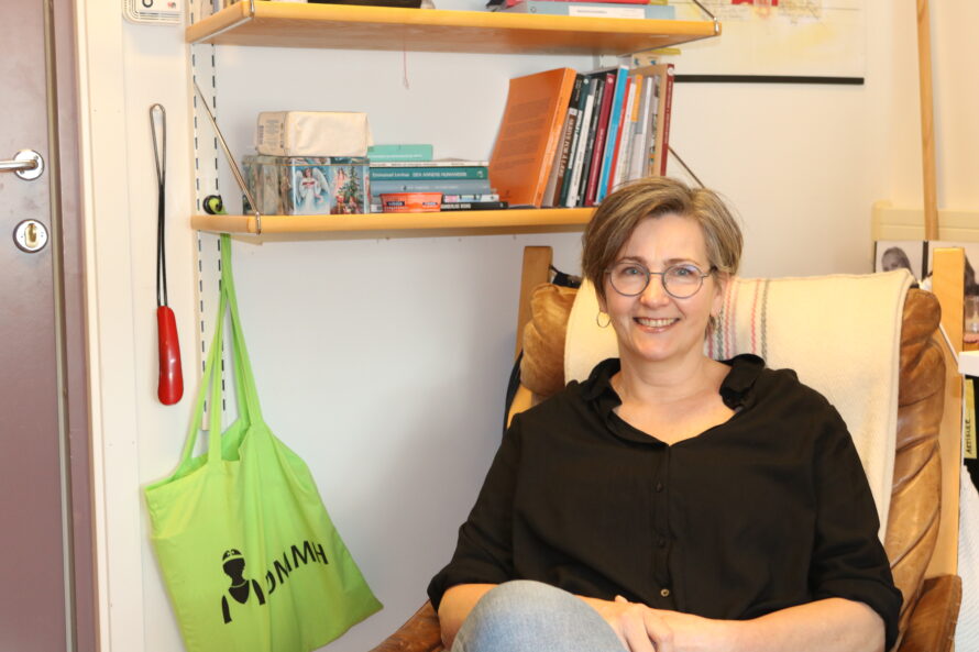 Bilde av en kvinne med briller som sitter foran en bokhylle.