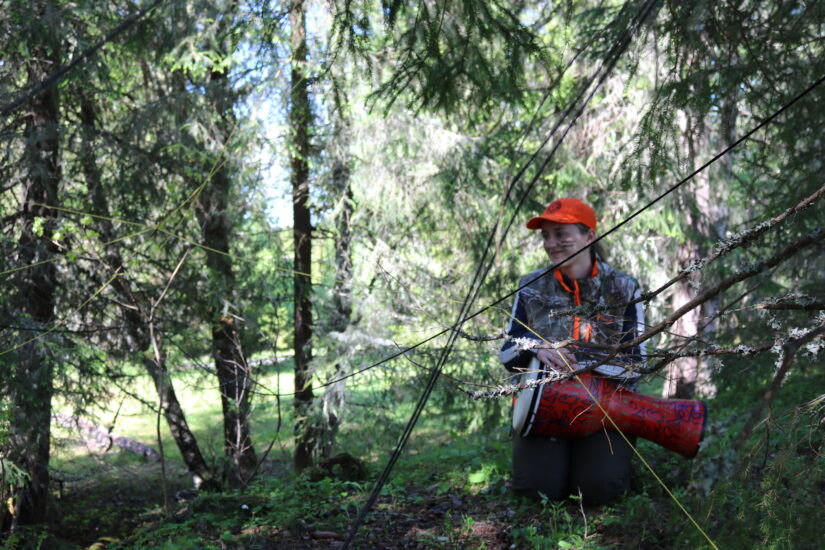En kvinen sitter i skogen med en tromme,
